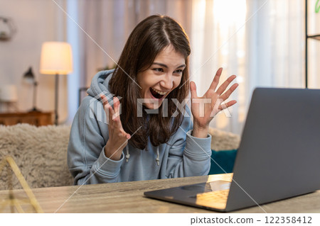 Happy woman sitting on sofa at table using laptop celebrating online victory or good news at home Happy woman sitting on sofa at table using laptop celebrating online victory or good news at home 122358412