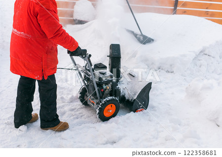 Closeup of red snow blower in action. Senior mature man outdoor in front of house using snowblower machine for removing snow on yard. Snow thrower in winter outside home. Young worker guy blowing snow 122358681