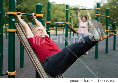 Elderly man doing exercises on a horizontal bar at an outdoor sports ground 122359400