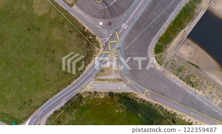 Aerial view of a road intersection with clear yellow and white markings, surrounded by greenery, pavement, and a nearby water body, showcasing detailed infrastructure planning. 122359487
