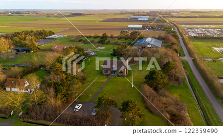 A scenic aerial view of a countryside house surrounded by lush green fields, trees, and farm buildings, with a pathway leading to the house under a partly cloudy sky. A scenic aerial view of a countryside house surrounded by lush green fields, trees, and farm buildings, with a pathway leading to the house under a partly cloudy sky. 122359490
