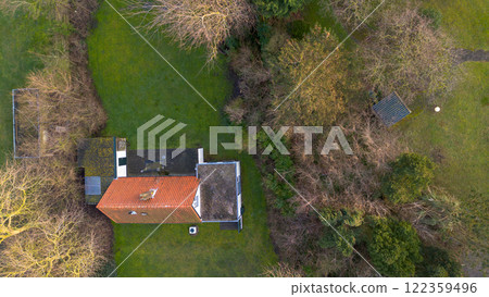 A scenic aerial view of a countryside house surrounded by lush green fields, trees, and farm buildings, with a pathway leading to the house under a partly cloudy sky. A scenic aerial view of a countryside house surrounded by lush green fields, trees, and farm buildings, with a pathway leading to the house under a partly cloudy sky. 122359496