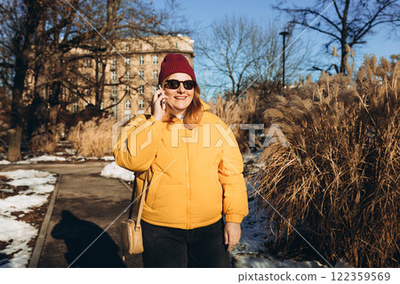 Happy 30s woman talking phone and look happy outdoors. Urban lifestyle concept. Winter time. Beautiful woman walking on the modern city public park. 122359569