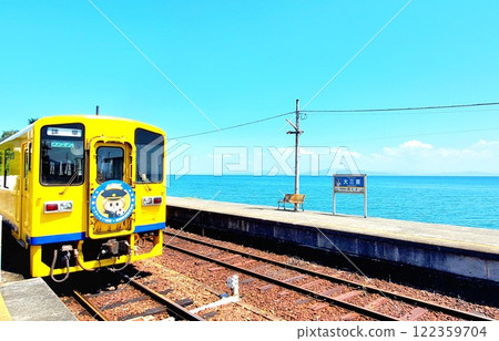 一列黃色火車沿著海岸線行駛，背景是藍色的大海和天空 122359704