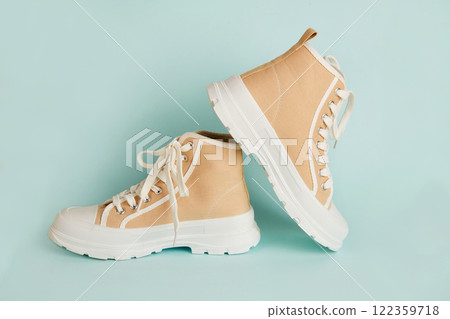 A pair of beige sneakers on an isolated blue background. Running shoes A pair of beige sneakers on an isolated blue background. Running shoes 122359718