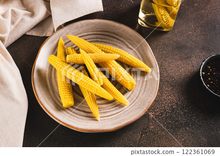 Portion of canned corn on the cob on a plate and in a jar on a table 122361069