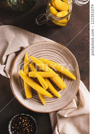 Portion of canned corn on the cob on a plate and in a jar on a table top and vertical view Portion of canned corn on the cob on a plate and in a jar on a table top and vertical view 122361074