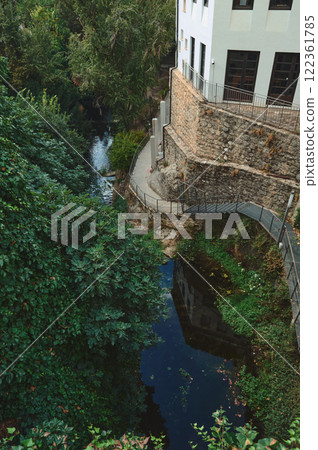 Scenic Riverside Pathway by a Historic Stone Building Surrounded by Lush Greenery 122361785