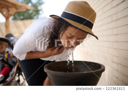 Woman drinking water from a fountain outdoors on a sunny day Woman drinking water from a fountain outdoors on a sunny day 122361811