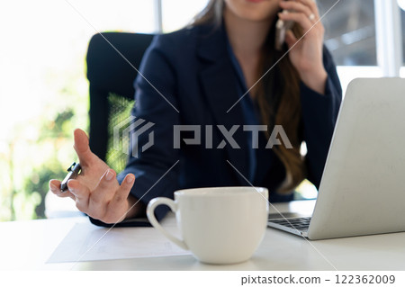 Businesswoman sitting at desk on couch in workplace or at home working on laptop and analyzing data on charts and graphs and writing on papers to make business plan and strategies for company. Businesswoman sitting at desk on couch in workplace or at home working on laptop and analyzing data on charts and graphs and writing on papers to make business plan and strategies for company. 122362009