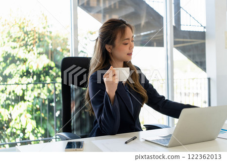 Businesswoman sitting at desk on couch in workplace or at home working on laptop and analyzing data on charts and graphs and writing on papers to make business plan and strategies for company. 122362013