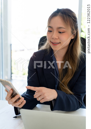 Businesswoman sitting at desk on couch in workplace or at home working on laptop and analyzing data on charts and graphs and writing on papers to make business plan and strategies for company. Businesswoman sitting at desk on couch in workplace or at home working on laptop and analyzing data on charts and graphs and writing on papers to make business plan and strategies for company. 122362015
