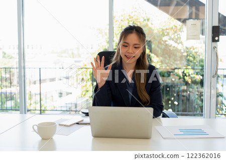 Businesswoman sitting at desk on couch in workplace or at home working on laptop and analyzing data on charts and graphs and writing on papers to make business plan and strategies for company. 122362016