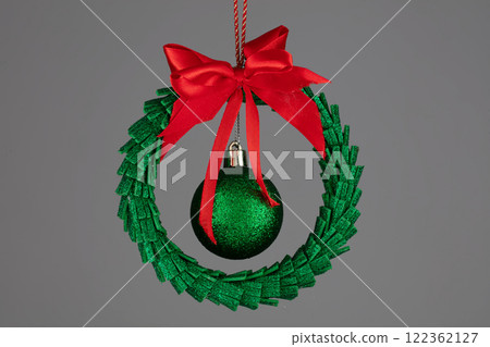 Green Christmas tree toy in the form of a garland with a ball and a red bow on a gray background. 122362127