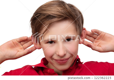 A teenage boy holds his ears with his hands and looks at the camera. 122362223