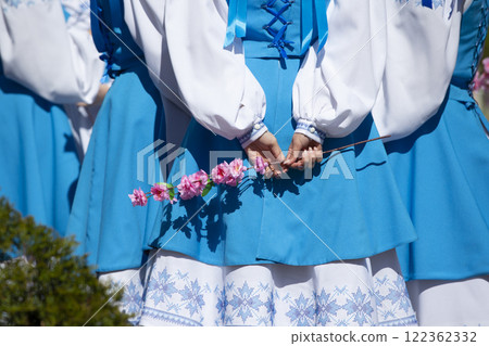 A girl in national Slavic clothes holds a flower behind her back A girl in national Slavic clothes holds a flower behind her back 122362332