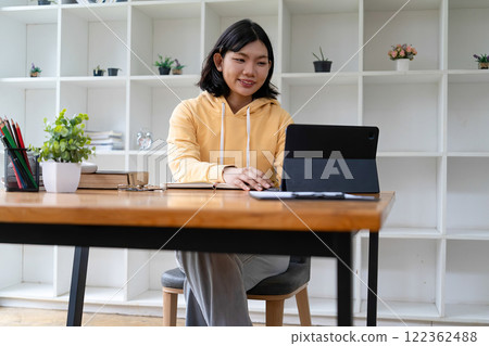 Intelligent young woman having online lessons on laptop, drinking coffee and taking notes, 122362488
