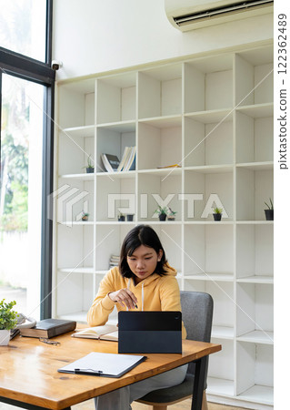 Intelligent young woman having online lessons on laptop, drinking coffee and taking notes, 122362489