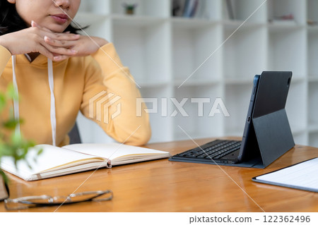 Intelligent young woman having online lessons on laptop, drinking coffee and taking notes, 122362496