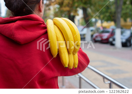 A woman holds a branch of bananas behind her back. 122362622