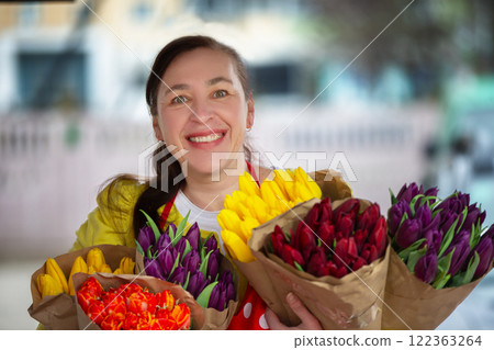 A female florist with bouquets of tulip flowers smiles and looks at the camera. A female florist with bouquets of tulip flowers smiles and looks at the camera. 122363264