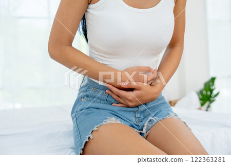 Front view and close up woman sit on bed and express of stomach ache by use two hands to hold her stomach in bedroom. 122363281