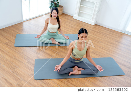 High view of two beautiful Asian women with exercise clothes do yoga posture like meditation in room with day light. High view of two beautiful Asian women with exercise clothes do yoga posture like meditation in room with day light. 122363302