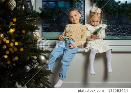 Happy children brother and sister are sitting on the window of the Christmas room. 122363434