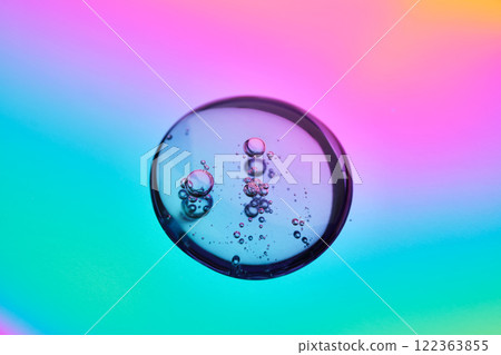 A drop of cosmetic serum on a multicolored background in shades of blue and lilac. A drop of cosmetic serum on a multicolored background in shades of blue and lilac. 122363855