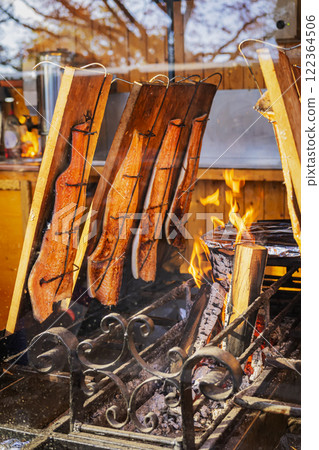 Salmon fillets roasting over open fire, outdoor market. Concept of traditional fish cooking, smoky flavor. Grilled fish Salmon fillets roasting over open fire, outdoor market. Concept of traditional fish cooking, smoky flavor. Grilled fish 122364506