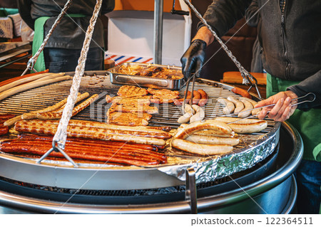 Chefs grill selection of sausages and meats, open flame, outdoor market, lively atmosphere filled with delicious aromas 122364511