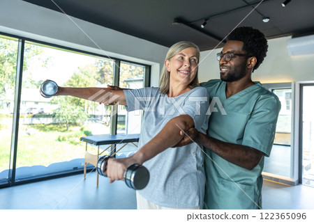 Man chiropractor in hospital assisting mature woman with pain relief exercises for physical recovery 122365096