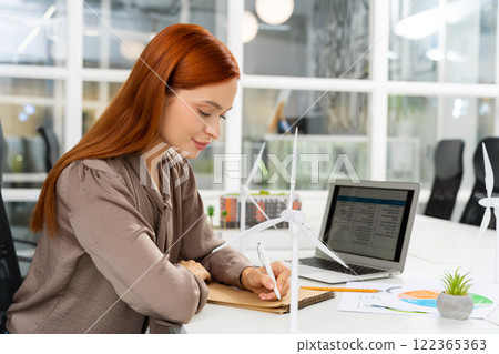 Ginger young woman working in the office on a new project of wind farm 122365363