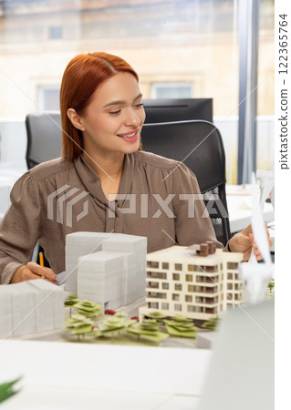 Young pretty woman sitting at the table and working on a building model 122365764
