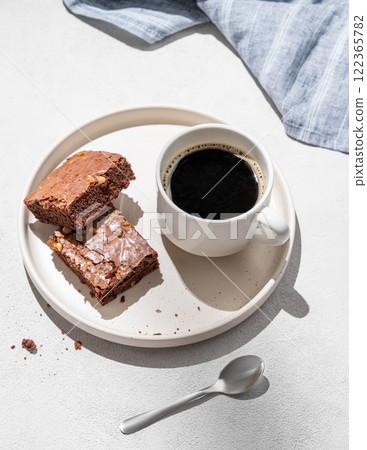 Pieces of chocolate brownie with nuts on a plate with a cup of espresso coffee on a light background Pieces of chocolate brownie with nuts on a plate with a cup of espresso coffee on a light background 122365782