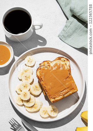 Peanut butter toast on a plate with banana on a light background with a cup of freshly brewed coffee Peanut butter toast on a plate with banana on a light background with a cup of freshly brewed coffee 122365788
