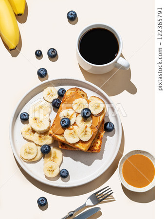 Flat lay of peanut butter toast with banana and blueberry on a plate on a beige background Flat lay of peanut butter toast with banana and blueberry on a plate on a beige background 122365791