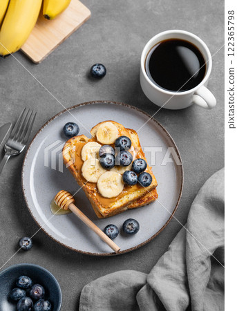 Peanut butter toast with banana, blueberry and honey on a plate on a dark  background 122365798