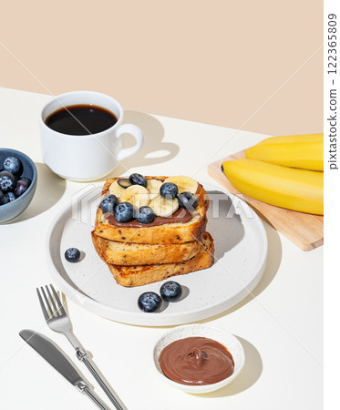 Toasted bread with chocolate cream, blueberries and banana on a plate on a light background 122365809