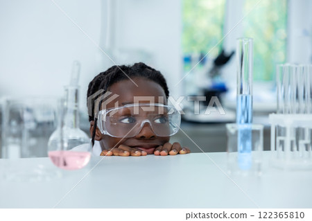 Scientist hiding behind table with petri dish and flask analyzing sample conducting research in laboratory 122365810