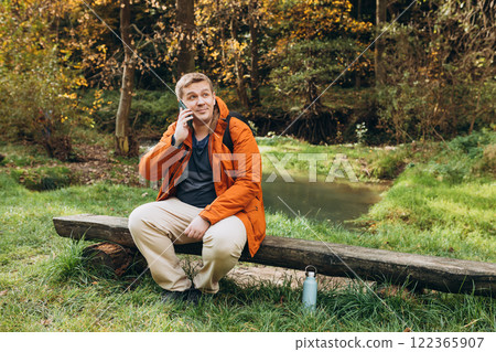 Handsome young man resting on a mountain trail and talking on the phone. Freedom and active lifestyle concept. High quality photo 122365907