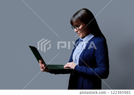 Middle aged business woman using laptop on grey background Middle aged business woman using laptop on grey background 122365981