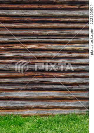 Weathered wooden logs creating rustic wall, revealing traditional russian architectural style amid verdant grassy landscape Weathered wooden logs creating rustic wall, revealing traditional russian architectural style amid verdant grassy landscape 122365994