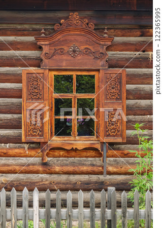 Ornate wooden window frame adorning traditional russian log cabin, framing verdant landscape and highlighting intricate woodworking artistry Ornate wooden window frame adorning traditional russian log cabin, framing verdant landscape and highlighting intricate woodworking artistry 122365995