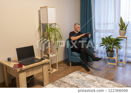 Man sitting in the cozy corner in the apartment on comfortable arm chair. 122366006