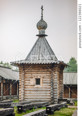Weathered wooden chapel standing tall with cross adorned roof, symbolizing spiritual legacy within rustic russian village landscape 122366021