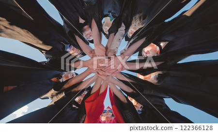 Recent graduates in cap and gown join hands in a circle 122366128