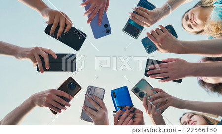 Group of friends using their smartphone forming a circle with their arms. 122366130