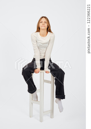 Young woman sitting on a stool, showcasing a casual and confident posture Young woman sitting on a stool, showcasing a casual and confident posture 122366221