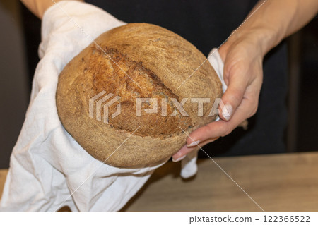 Woman holds freshly baked loaf of rye bread on the linen cloth Woman holds freshly baked loaf of rye bread on the linen cloth 122366522